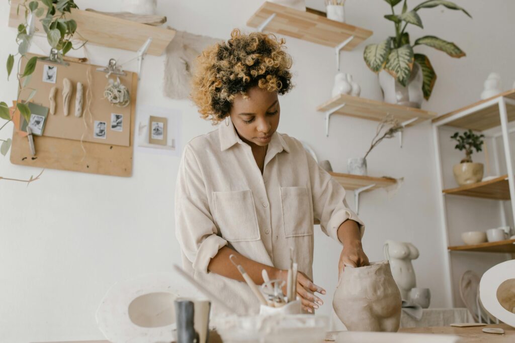 Creative artisan shaping clay in a serene workshop, surrounded by earthenware and plants.